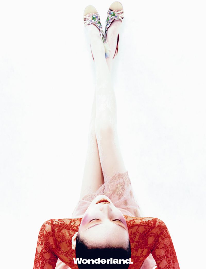 Overhead shot of a woman in red lace top and pink floral sandals with her legs raised against a bright white background.