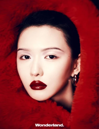 Close-up studio portrait of an Asian adult female with dark hair and bold red lipstick, posing in front of a textured red background.
