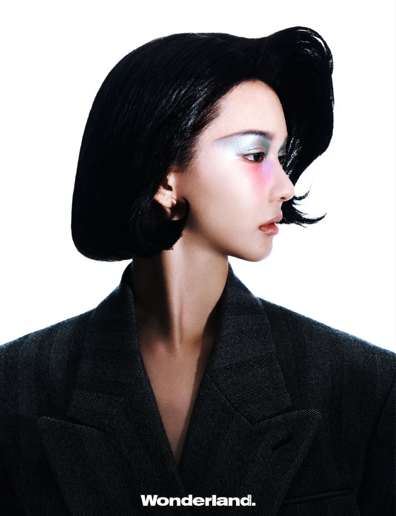 Profile shot of a stylish Asian woman with a black bob haircut, silver eyeshadow, a grey blazer, and clean white background.
