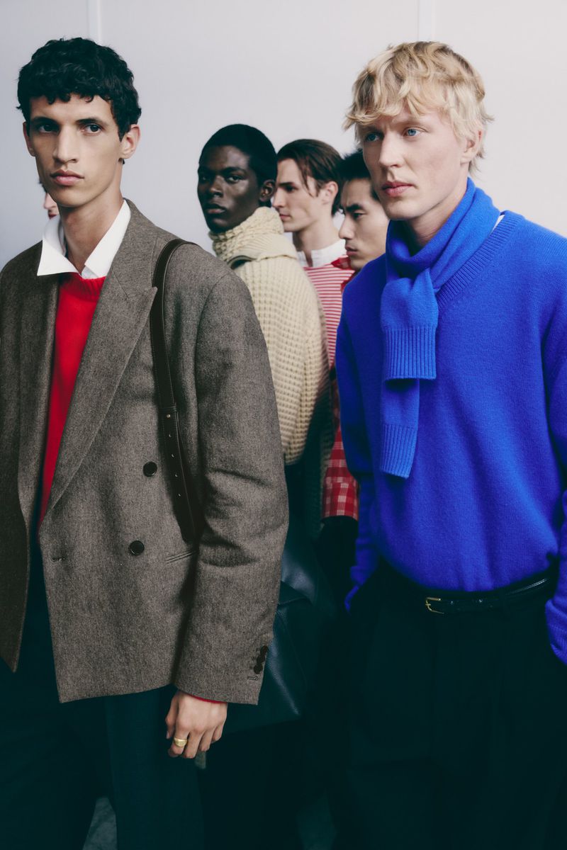 Fashion shot of a group of five male models in an indoor setting, wearing sweaters and jackets, posing in a line.