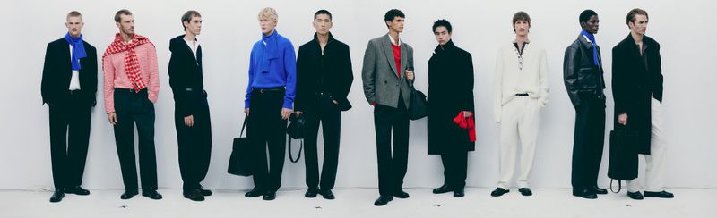Multiple male fashion models in indoor studio showcase full-length outfits against white backdrop, featuring diverse styles and accessories.