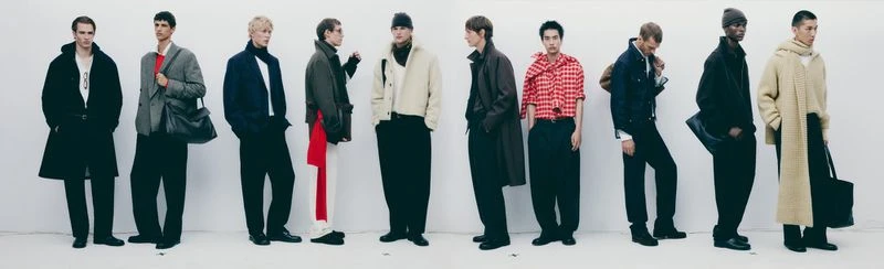 Group of male fashion models in various fall and winter coats stand against a neutral backdrop, showcasing menswear apparel.