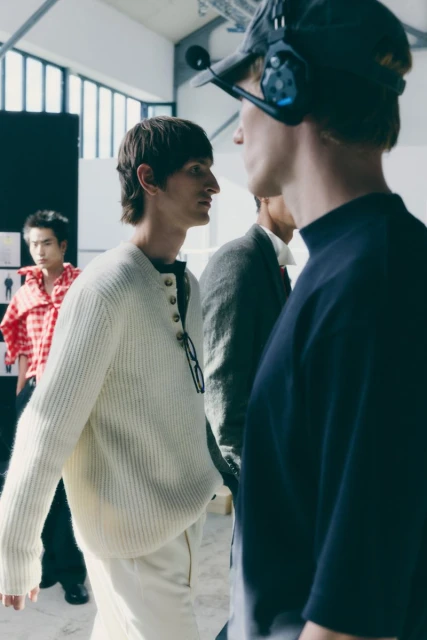 Candid shot of several people indoors at a fashion photography shoot with a neutral color palette and natural lighting.