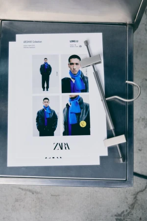 Fashion images on metal table display: men wearing scarfs and jackets, ZARA logo visible, indoor fashion editorial presentation.