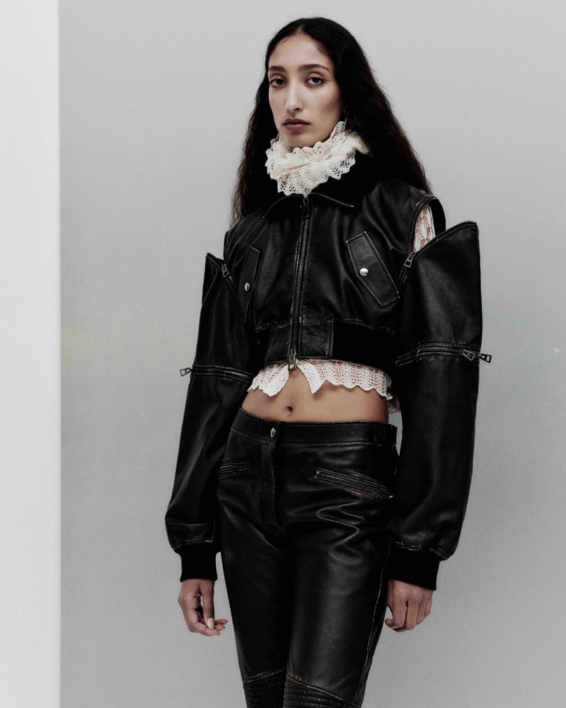 A woman in a black leather jacket and pants poses in a studio with a lace collar, creating a high fashion editorial shot.