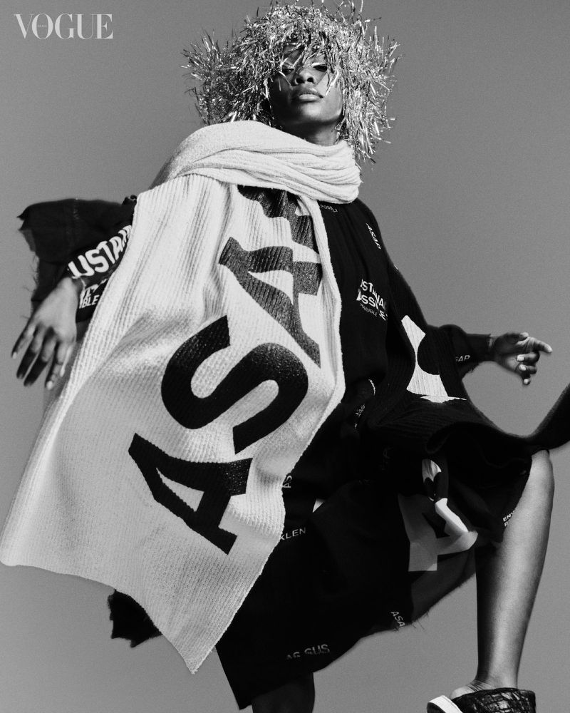 Black and white fashion editorial portrait of an adult male wearing a silver headpiece and draped with a white patterned scarf.