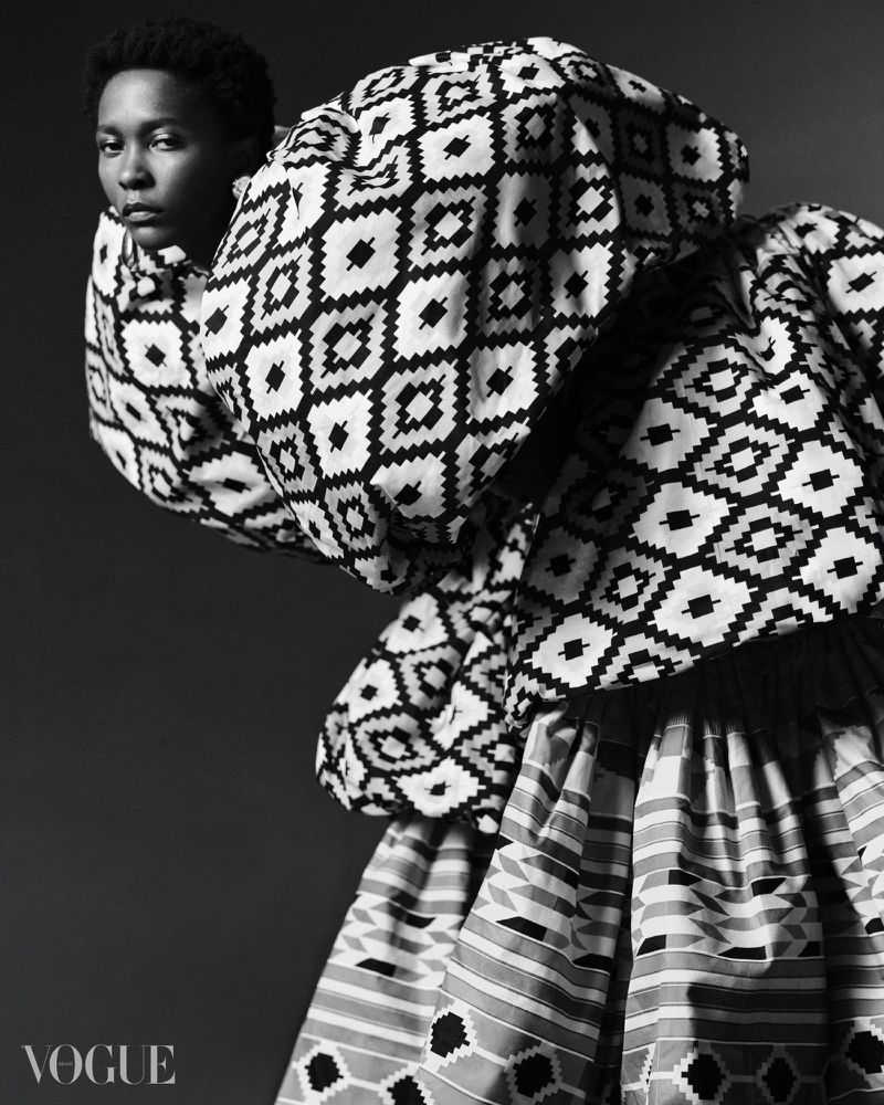 Black and white portrait of a Black female model in patterned high-fashion garment and Vogue logo at bottom left.