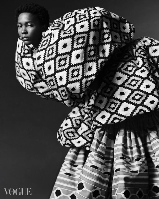Black and white portrait of a Black female model in patterned high-fashion garment and Vogue logo at bottom left.