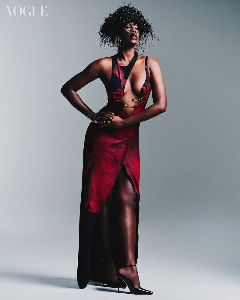 Full-length studio shot of a Black woman in a long red dress with a high slit, paired with black high heels, posing against a neutral background.