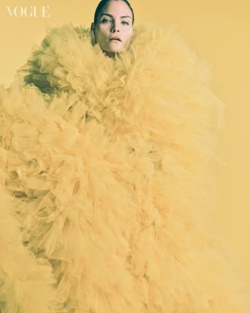 Fashion editorial shot of an adult woman in a large, frilly, yellow tulle dress against a matching yellow background in the photo studio.