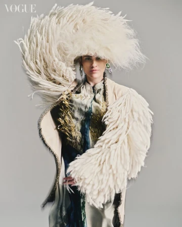 Fashion editorial shot of a woman wearing an extravagant feathered hat and coat in a studio setting, highlighting avant-garde design and texture.