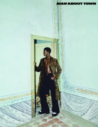 Man wearing a leopard-print coat and black trousers standing in an ornate doorway for Man About Town.