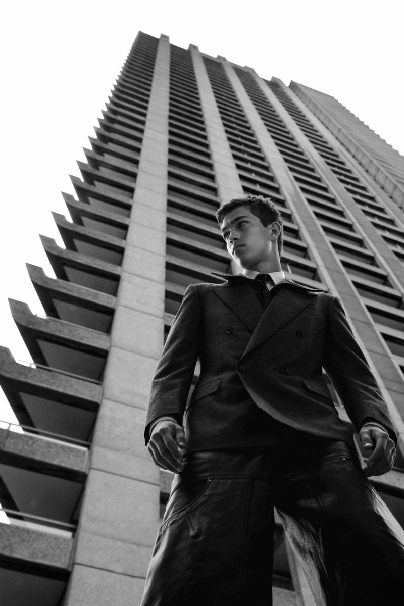 Low-angle shot of a stylish adult male in a suit against a tall building, creating a striking monochrome fashion portrait.