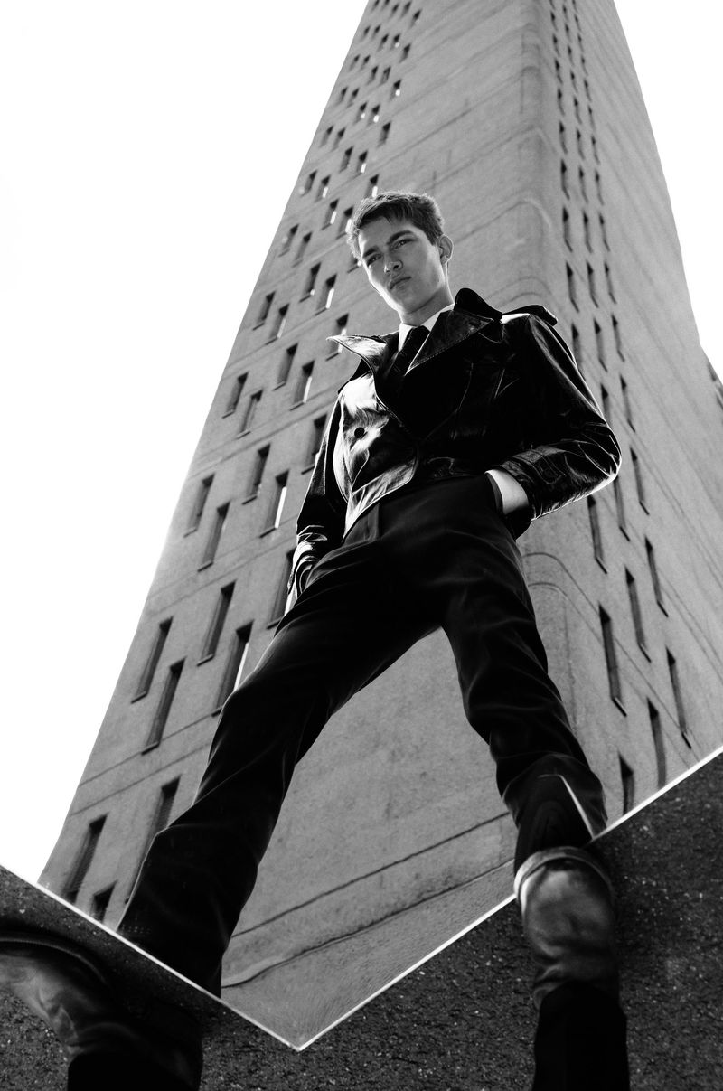 Monochrome portrait of a male fashion model posing in front of a high-rise building, shot from a low angle for a powerful perspective.