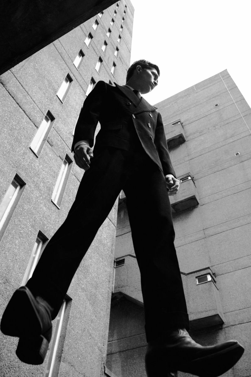 Monochrome low-angle shot of an adult male in a suit walking, with tall buildings in the background, creating a unique and striking visual.