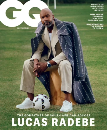 GQ magazine cover featuring Lucas Radebe, the South African soccer icon, wearing a beige suit and patterned coat, seated with a soccer ball.