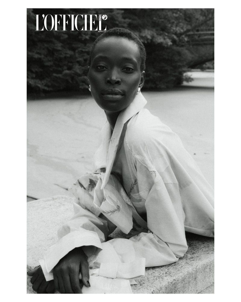 Black and white portrait of a Black female model wearing a white collared shirt in a garden, as featured in L'Officiel magazine.