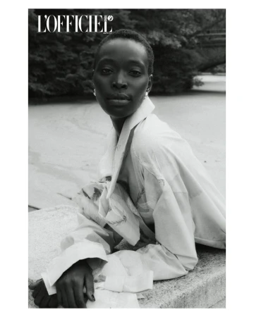 Black and white portrait of a Black female model wearing a white collared shirt in a garden, as featured in L'Officiel magazine.