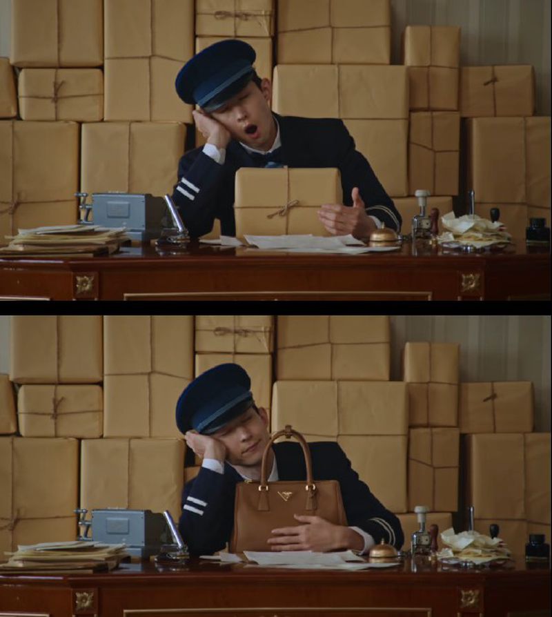 Man in uniform at desk napping among stacked boxes. He is resting on a purse in the bottom half of the image.