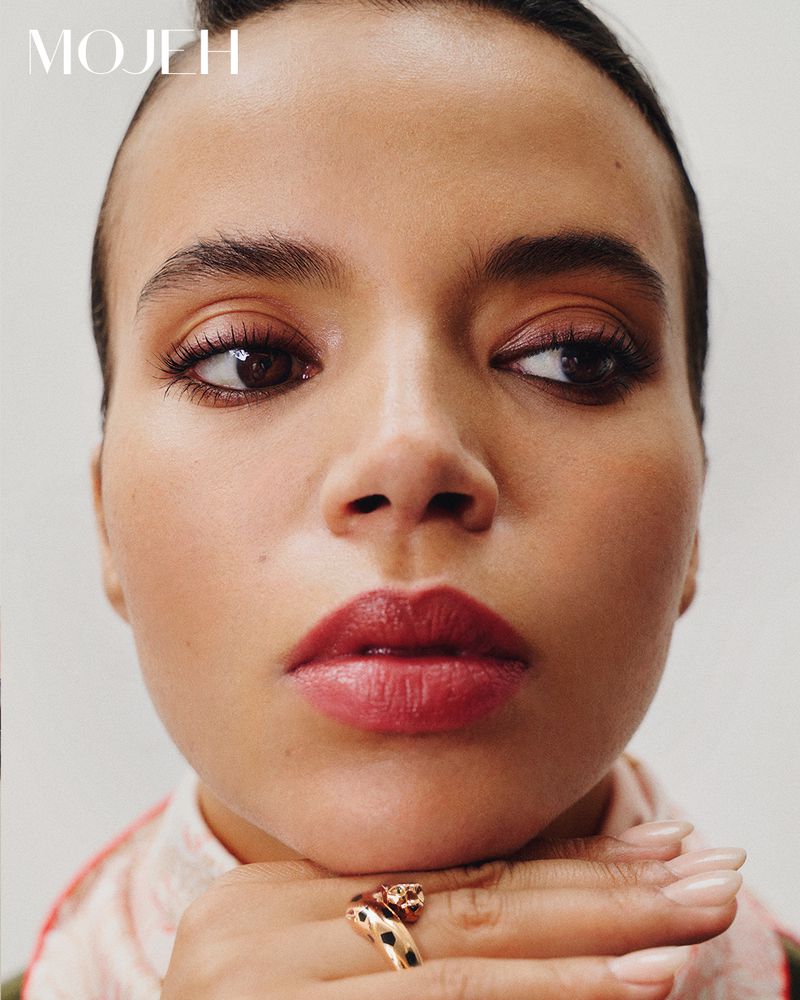 Close-up studio portrait of an adult female with hand under chin, wearing a gold ring, glossy red lipstick, and natural makeup.