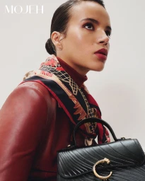 Model Calista Choley in a red leather jacket and printed silk scarf posing with a black structured leather handbag.