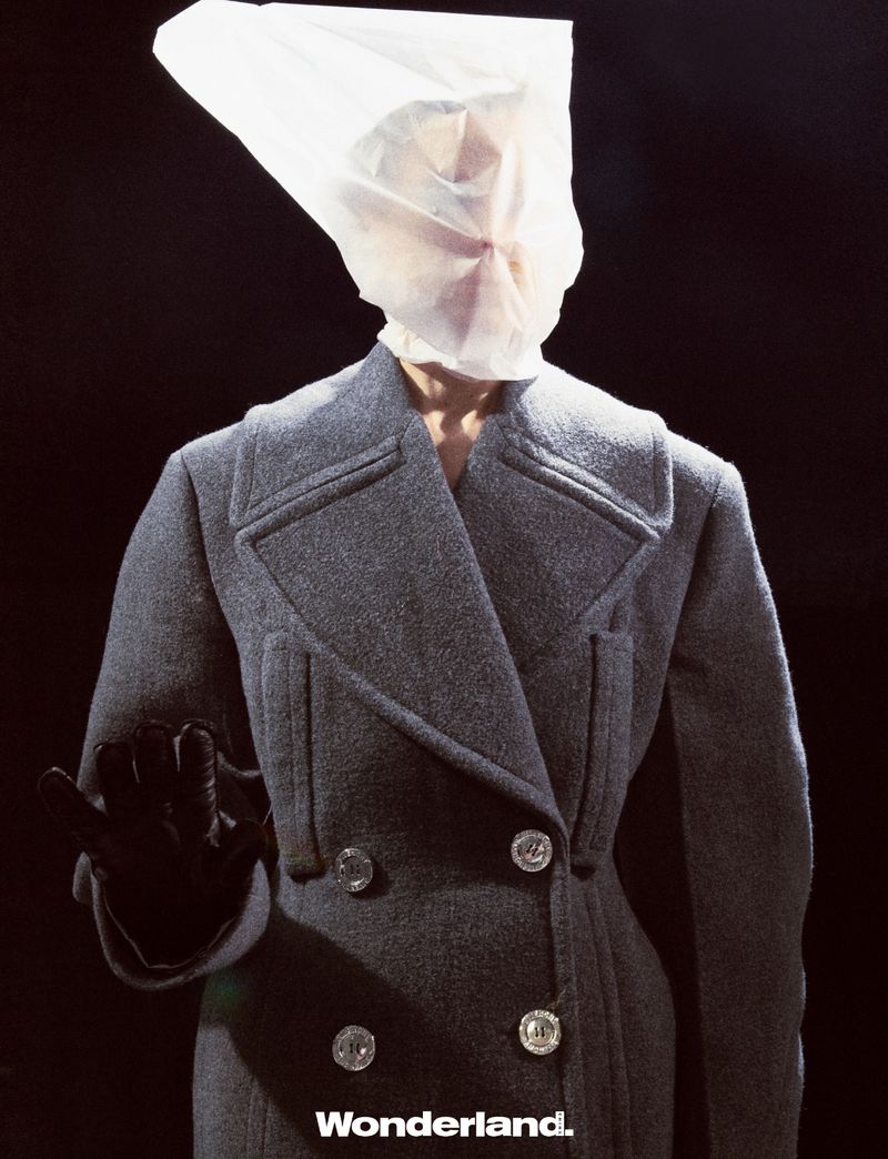 Fashion shot of person in grey coat with bag over head in front of a black background. The word Wonderland is at the bottom.