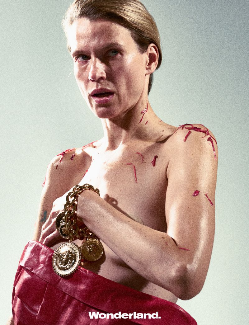 Adult posing with red bag and gold chain necklace, dramatic light, editorial fashion shot. Wonderland. logo visible at bottom.