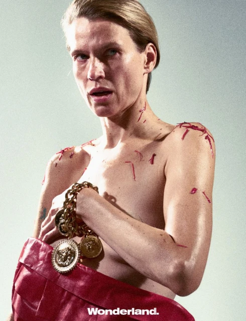 Adult posing with red bag and gold chain necklace, dramatic light, editorial fashion shot. Wonderland. logo visible at bottom.