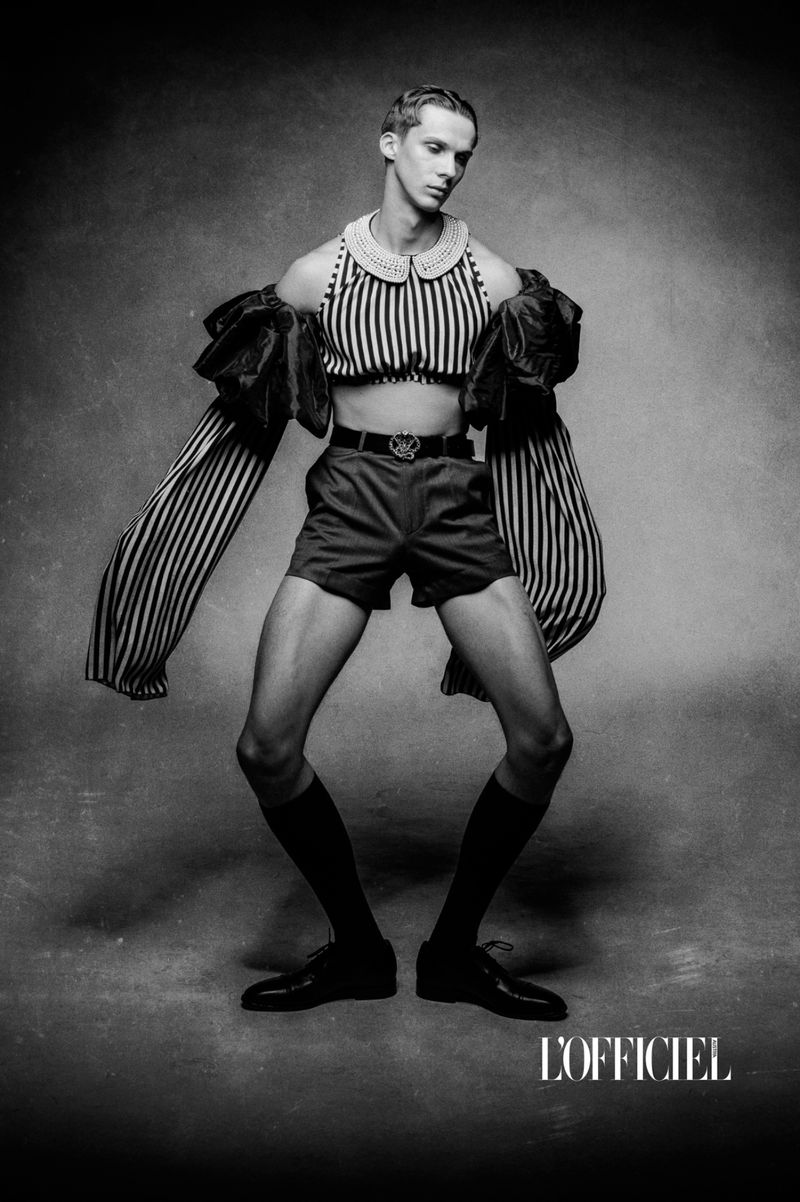Fashion photo features a slender person in a striped crop top and shorts, posing in front of a mottled grey background with dramatic sleeves.