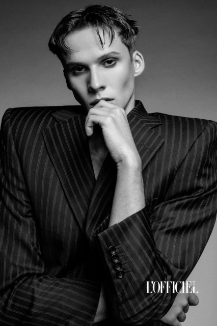 Monochrome portrait of a young adult male model wearing a pinstripe blazer, looking directly at the camera with a neutral expression.