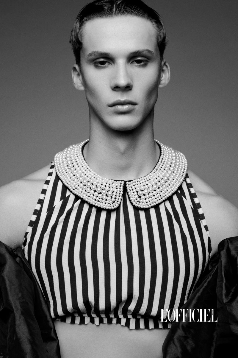 Monochrome portrait of a young adult male with short hair, wearing a striped halter top and a pearl-embellished Peter Pan collar.