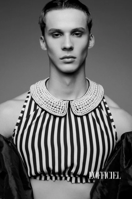 Monochrome portrait of a young adult male with short hair, wearing a striped halter top and a pearl-embellished Peter Pan collar.