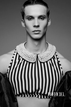 Monochrome portrait of a young adult male with short hair, wearing a striped halter top and a pearl-embellished Peter Pan collar.