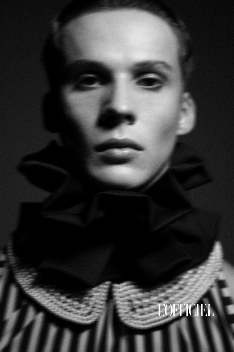 Portrait of a fashion model in a striped shirt and ruffled collar, shot in black and white, with a dark background and the 'L'Officiel' logo.