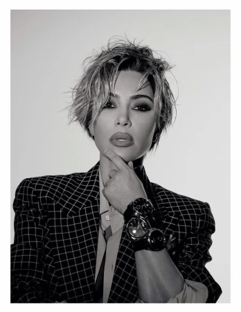 Black and white portrait of an adult female with short hair wearing a checked blazer and multiple watches, gazing directly at the viewer.