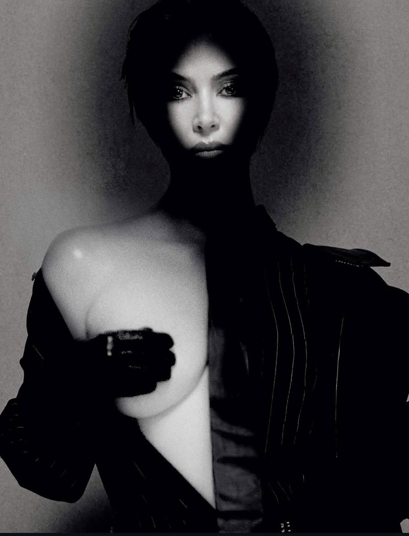 Striking black and white studio portrait of a woman with short hair in dramatic lighting, wearing a pinstripe suit and gloves.
