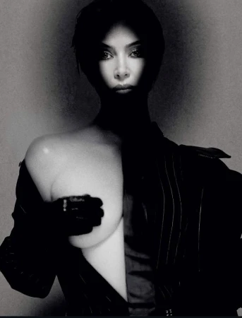 Striking black and white studio portrait of a woman with short hair in dramatic lighting, wearing a pinstripe suit and gloves.