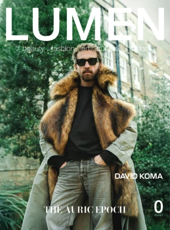 Man wearing sunglasses and a faux-fur trimmed coat standing outdoors against a residential building backdrop