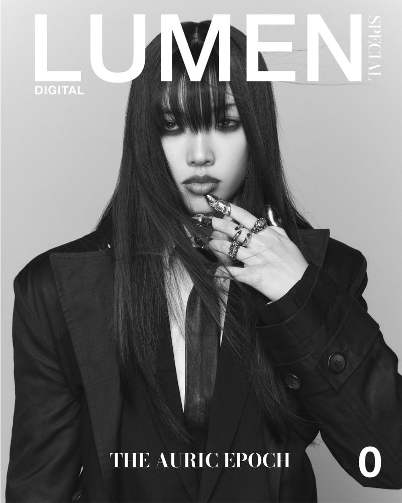 Black-and-white magazine cover featuring a woman with long dark hair wearing a black jacket and tie, with visible jewelry and makeup.