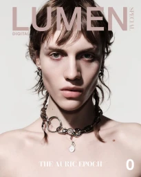 Portrait of a model wearing a heavy silver chain necklace against a light grey seamless backdrop for Lumen Spring 2025.