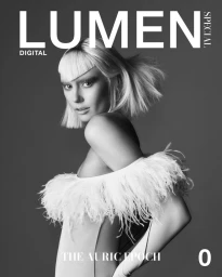 Black and white portrait of a model with feathered shoulders wearing a blunt-cut fringe hairstyle against a grey background.