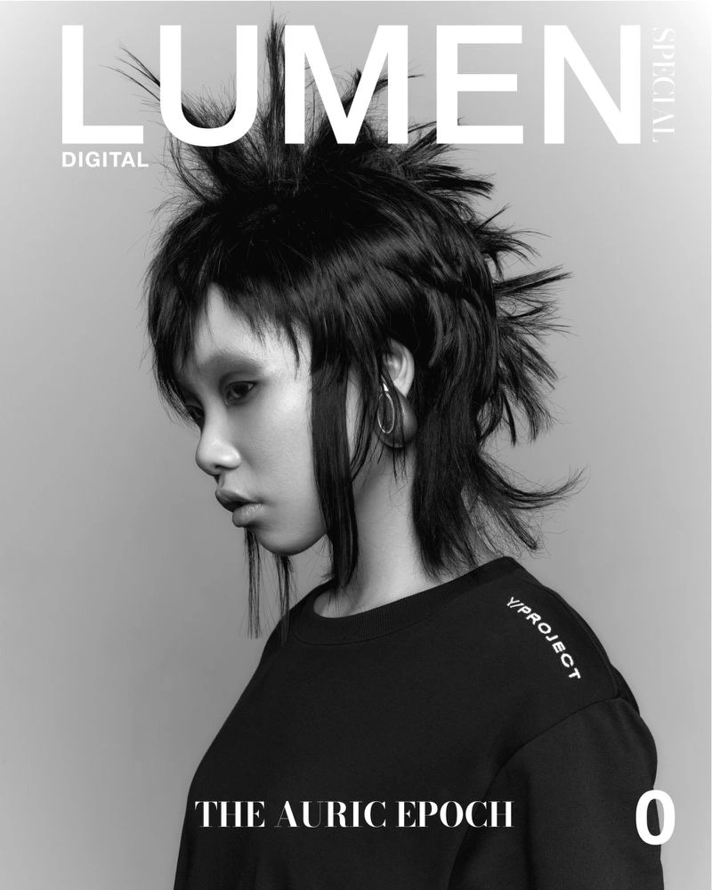 Monochrome magazine cover portrait of a model with spiky dark hair wearing a black top against a seamless grey studio background.