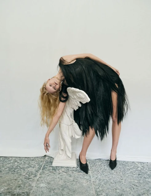 Fashionable model strikes an artistic pose with sculpture in a studio setting, showcasing an avant-garde dress and sharp heels.