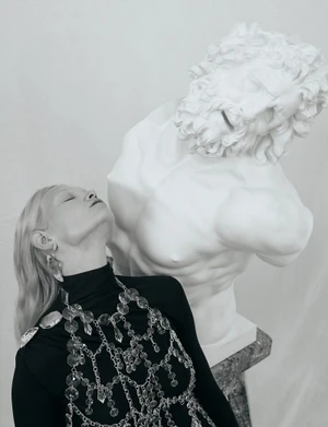 Model in black top and crystal body jewelry posing beside a white classical bust for Numéro Switzerland editorial