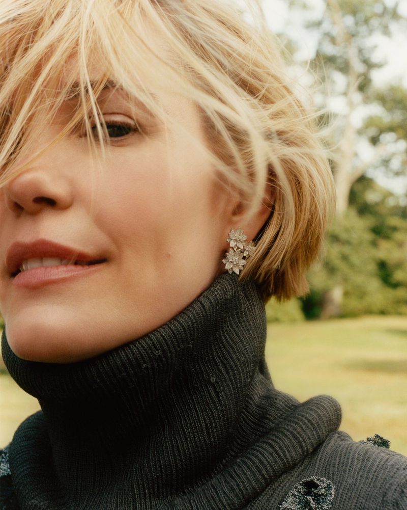 Leslie Bibb in a dark ribbed turtleneck sweater wearing sparkling floral cluster earrings in an outdoor portrait.
