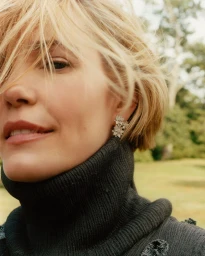 Leslie Bibb in a dark ribbed turtleneck sweater wearing sparkling floral cluster earrings in an outdoor portrait.