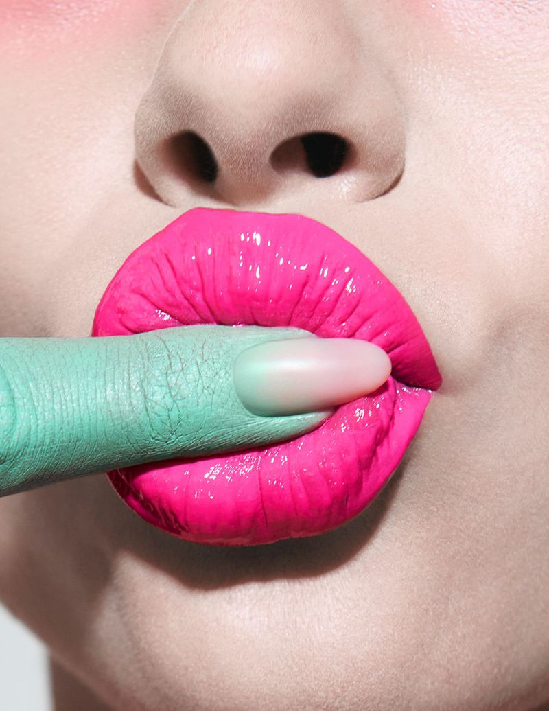 Close-up of vibrant hot pink glossy lips with a mint green painted finger resting between them.