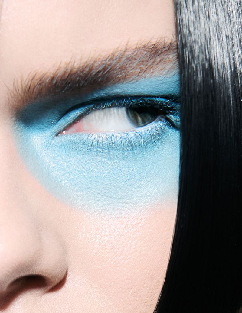 Close-up of a person's face with blue eyeshadow, black hair, and fair skin in a beauty shot emphasizing makeup and facial features.