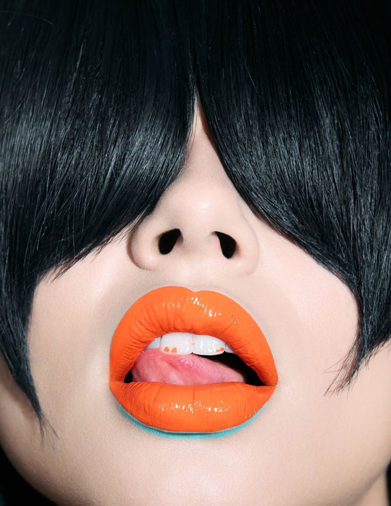 Close-up beauty shot of a model with black fringe bangs and glossy vibrant orange lipstick for Kaltblut Magazine.
