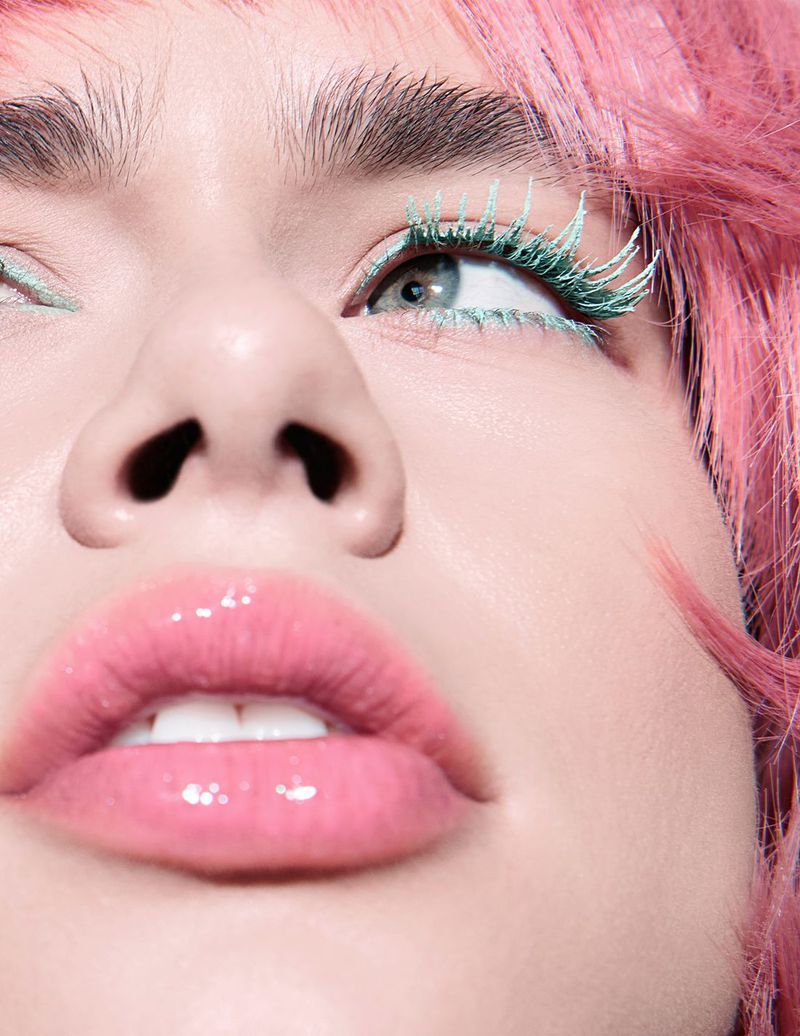 Close-up shot of a woman with pink hair and green eyelashes and eyeliner, looking upward, beauty and makeup fashion concept.